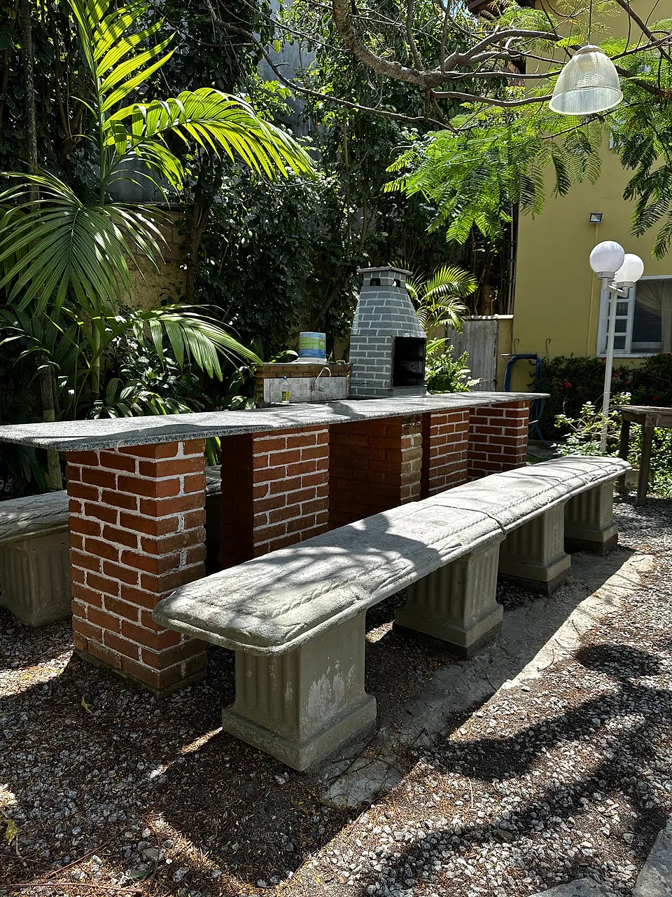 Área de churrasco com bancada e bancos de alvenaria entre plantas